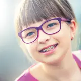 Uśmiechnięta dziewczynka w okularach i z aparatem ortodontycznym dla dzieci.