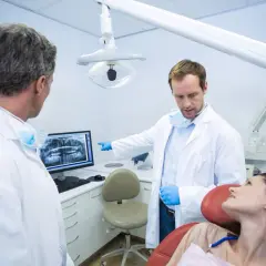 Dwóch dentystów omawia zdjęcie rentgenowskie z pacjentką, zastanawiając się, ile zarabia dentysta NFZ.