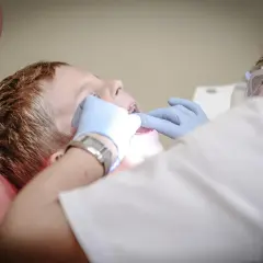 Chłopiec w gabinecie dentystycznym, któremu dentysta bada zęby. Może to być pomocne przy bólu zęba, jak szałwia.