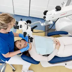 Dentystka pod mikroskopem bada ząb pacjentki. Czy leczenie kanałowe boli? Nowoczesna stomatologia minimalizuje dyskomfort.