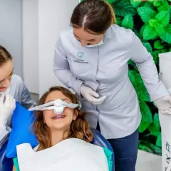 Uśmiechnięta dziewczynka z aparatem na zębach otrzymuje gaz rozweselający od dentystki, która obsługuje aparat.