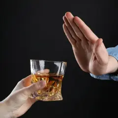 Ręka odrzuca szklankę z bursztynowym płynem. Czy dzień przed wizytą u dentysty można pić alkohol? Lepiej nie ryzykować.