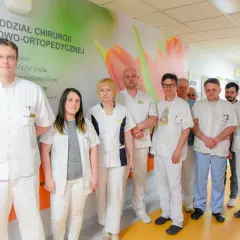 Grupa lekarzy w białych fartuchach stoi w szpitalnym korytarzu.