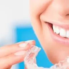 Uśmiechnięta kobieta trzymająca przezroczyste nakładki. Dowiedz się, co to Invisalign i jak działa.