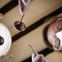 Dentysta w masce i rękawiczkach trzyma narzędzia. Zastanawiasz się, ile kosztuje znieczulenie u dentysty?