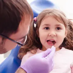 Mała dziewczynka u dentysty, który wykonuje lapisowanie zębów.