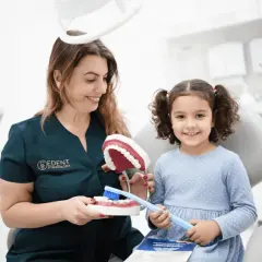 Dentystka uczy dziewczynkę higieny jamy ustnej, pokazując jak dbać o zęby, by miały mocny **hydroksyapatyt**.