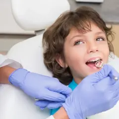 Chłopiec u dentysty, który sprawdza, kiedy wypadają mleczne 4. Zęby są zdrowe, a wizyta przebiega bezboleśnie.