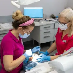 Dwie dentystki w maskach pracują przy pacjencie. Zastanawiasz się, ile schodzi znieczulenie od dentysty?