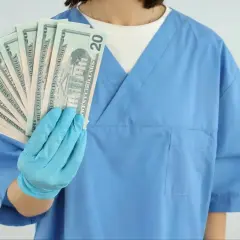 Higienistka stomatologiczna w niebieskim fartuchu pokazuje banknoty dwudziestodolarowe. Zastanawiasz się, ile zarabia higienistka stomatologiczna?