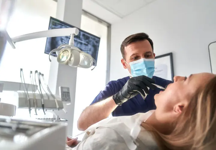 Dentysta w masce wykonuje zabieg szynowania zębów u pacjentki.