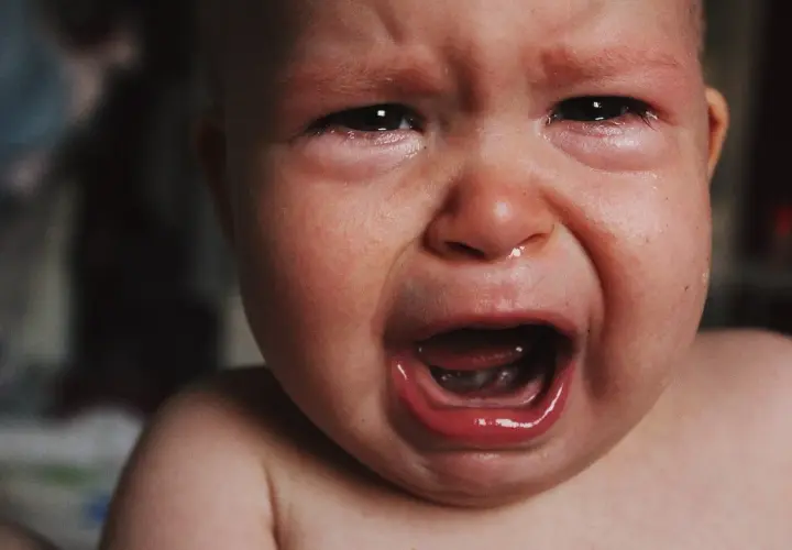 Malutkie dziecko płacze, ma zaczerwienione oczy i mokry nosek. To pewnie katar przy ząbkowaniu, który sprawia mu ból.