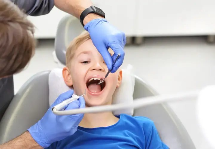 Chłopiec uśmiecha się szeroko, gdy dentysta wykonuje fluoryzację w szkole, dbając o zdrowe zęby.