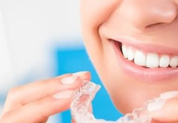 Uśmiechnięta kobieta trzymająca przezroczyste nakładki. Dowiedz się, co to Invisalign i jak działa.
