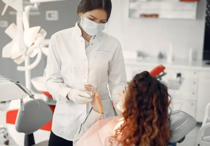 Dentystka w masce podaje wodę pacjentce. Bezpieczne leczenie kanałowe w ciąży jest możliwe.