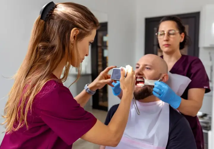 Dentystka z asystentką badają uśmiech pacjenta, by ocenić, jak długo osiada proteza zębowa.