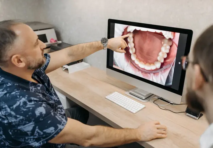 Dentysta pokazuje pacjentowi na ekranie powiększony obraz jamy ustnej, wskazując na zdrową kieszonkę dziąsłową.