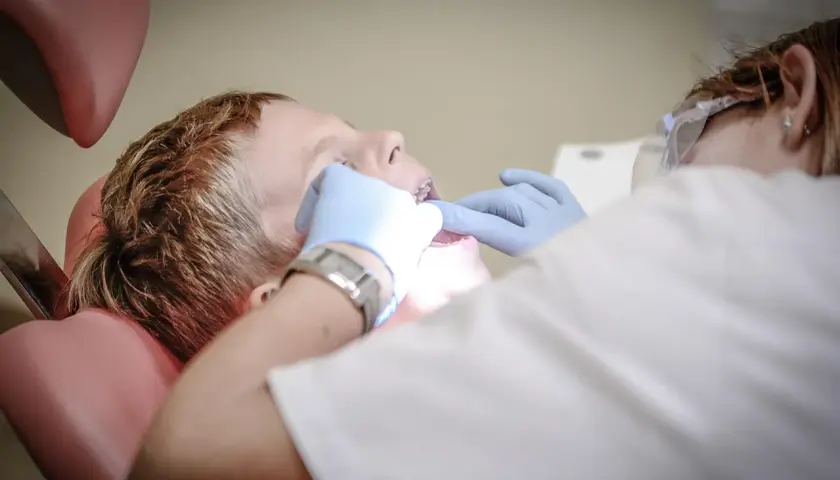 Chłopiec w gabinecie dentystycznym, któremu dentysta bada zęby. Może to być pomocne przy bólu zęba, jak szałwia.