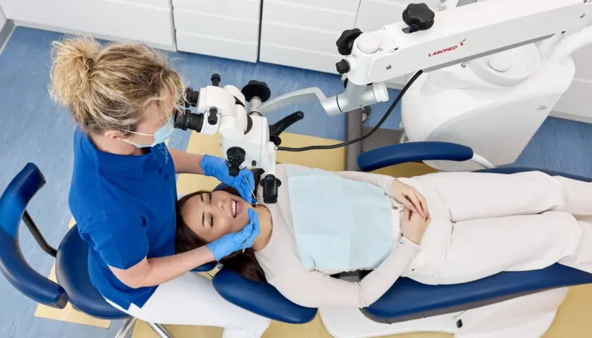 Dentystka pod mikroskopem bada ząb pacjentki. Czy leczenie kanałowe boli? Nowoczesna stomatologia minimalizuje dyskomfort.