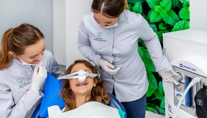 Uśmiechnięta dziewczynka z aparatem na zębach otrzymuje gaz rozweselający od dentystki, która obsługuje aparat.