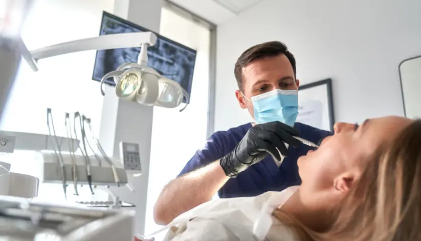 Dentysta w masce wykonuje zabieg szynowania zębów u pacjentki.