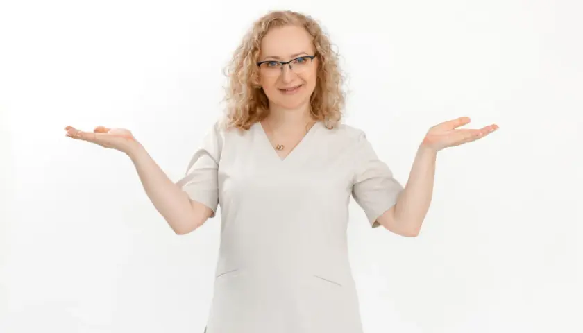 Kobieta w okularach i jasnym uniformie medycznym z otwartymi dłońmi.