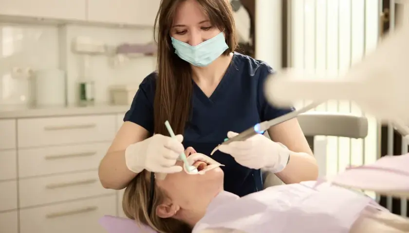 Dentystka w masce i rękawiczkach wykonuje zabieg. Szukasz najlepszych klinik stomatologicznych w Warszawie?
