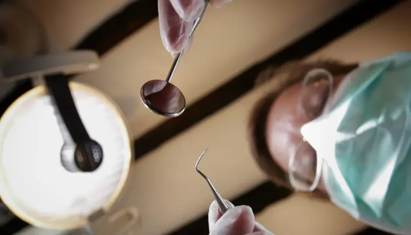 Dentysta w masce i rękawiczkach trzyma narzędzia. Zastanawiasz się, ile kosztuje znieczulenie u dentysty?