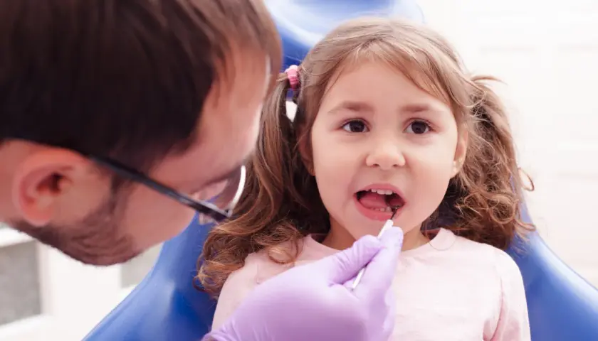 Mała dziewczynka u dentysty, który wykonuje lapisowanie zębów.