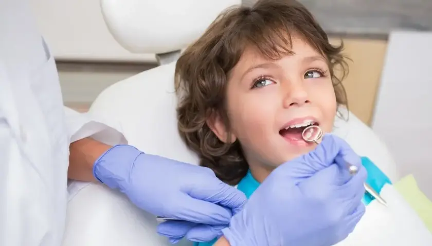 Chłopiec u dentysty, który sprawdza, kiedy wypadają mleczne 4. Zęby są zdrowe, a wizyta przebiega bezboleśnie.