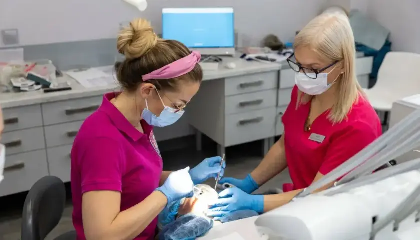 Dwie dentystki w maskach pracują przy pacjencie. Zastanawiasz się, ile schodzi znieczulenie od dentysty?
