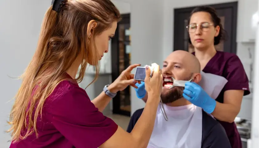 Dentystka z asystentką badają uśmiech pacjenta, by ocenić, jak długo osiada proteza zębowa.