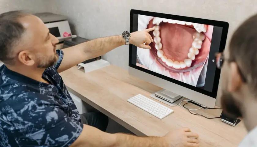 Dentysta pokazuje pacjentowi na ekranie powiększony obraz jamy ustnej, wskazując na zdrową kieszonkę dziąsłową.
