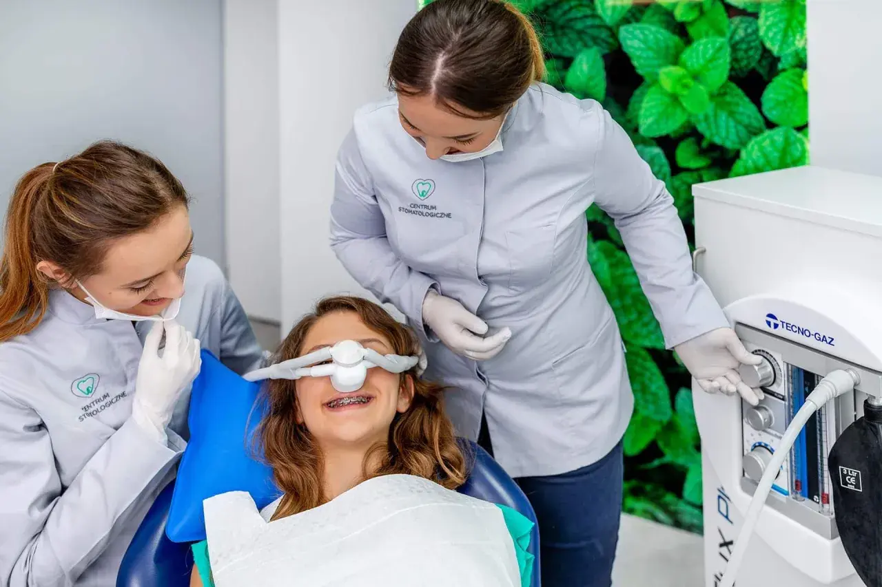 Uśmiechnięta dziewczynka z aparatem na zębach otrzymuje gaz rozweselający od dentystki, która obsługuje aparat.