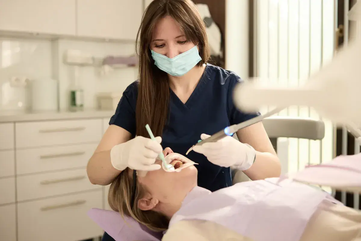 Dentystka w masce i rękawiczkach wykonuje zabieg. Szukasz najlepszych klinik stomatologicznych w Warszawie?