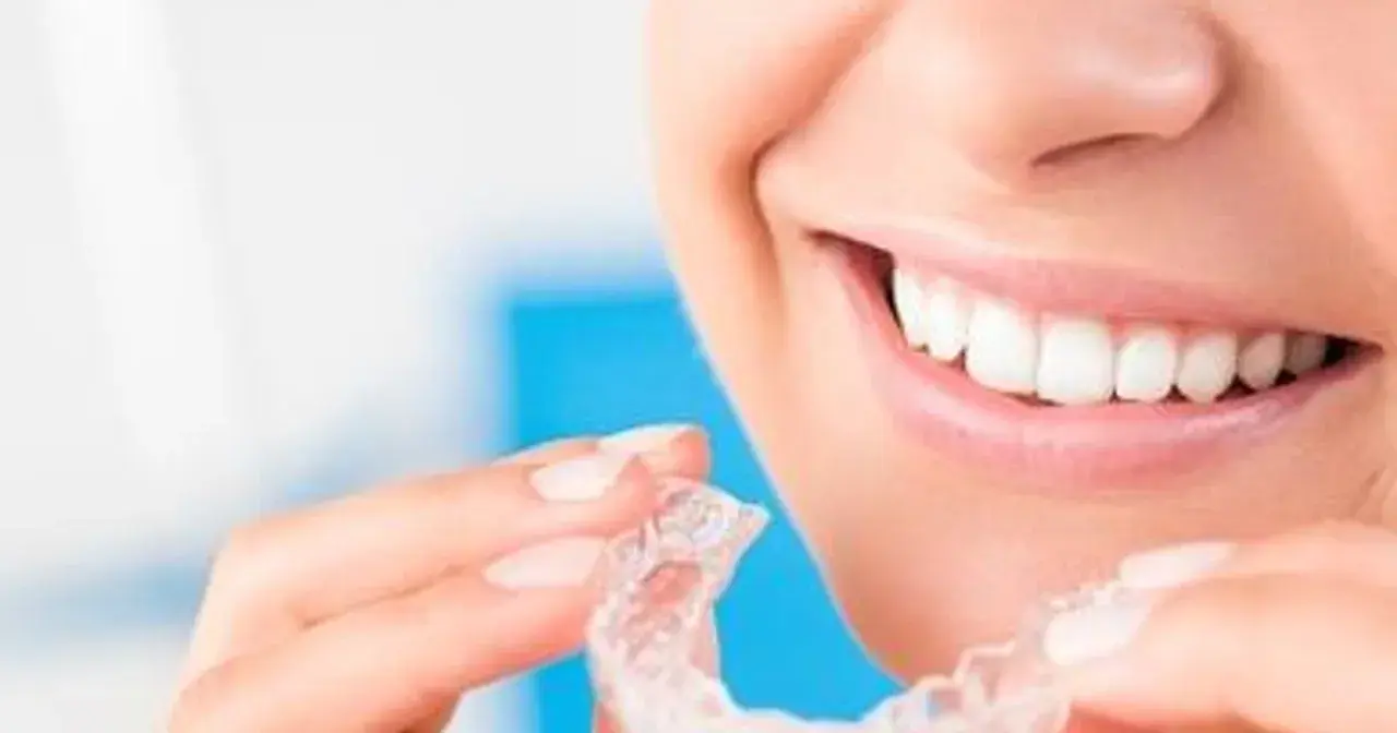 Uśmiechnięta kobieta trzymająca przezroczyste nakładki. Dowiedz się, co to Invisalign i jak działa.