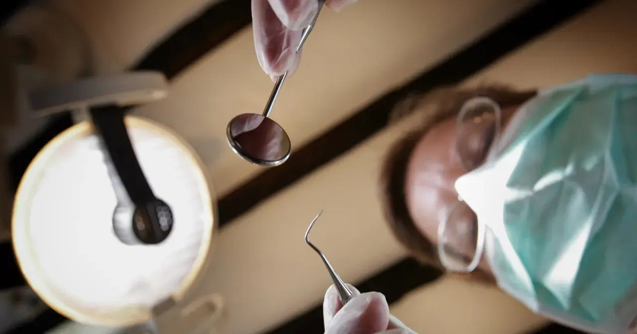 Dentysta w masce i rękawiczkach trzyma narzędzia. Zastanawiasz się, ile kosztuje znieczulenie u dentysty?