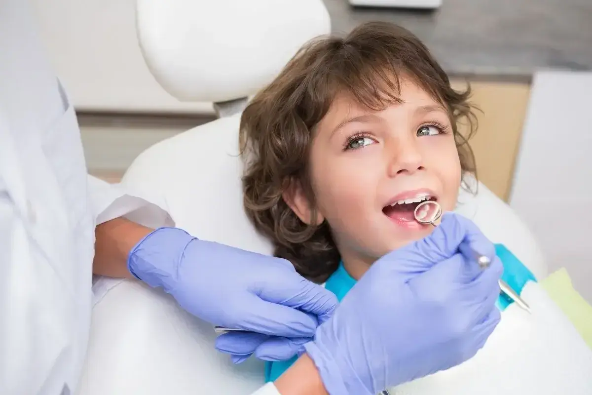Chłopiec u dentysty, który sprawdza, kiedy wypadają mleczne 4. Zęby są zdrowe, a wizyta przebiega bezboleśnie.