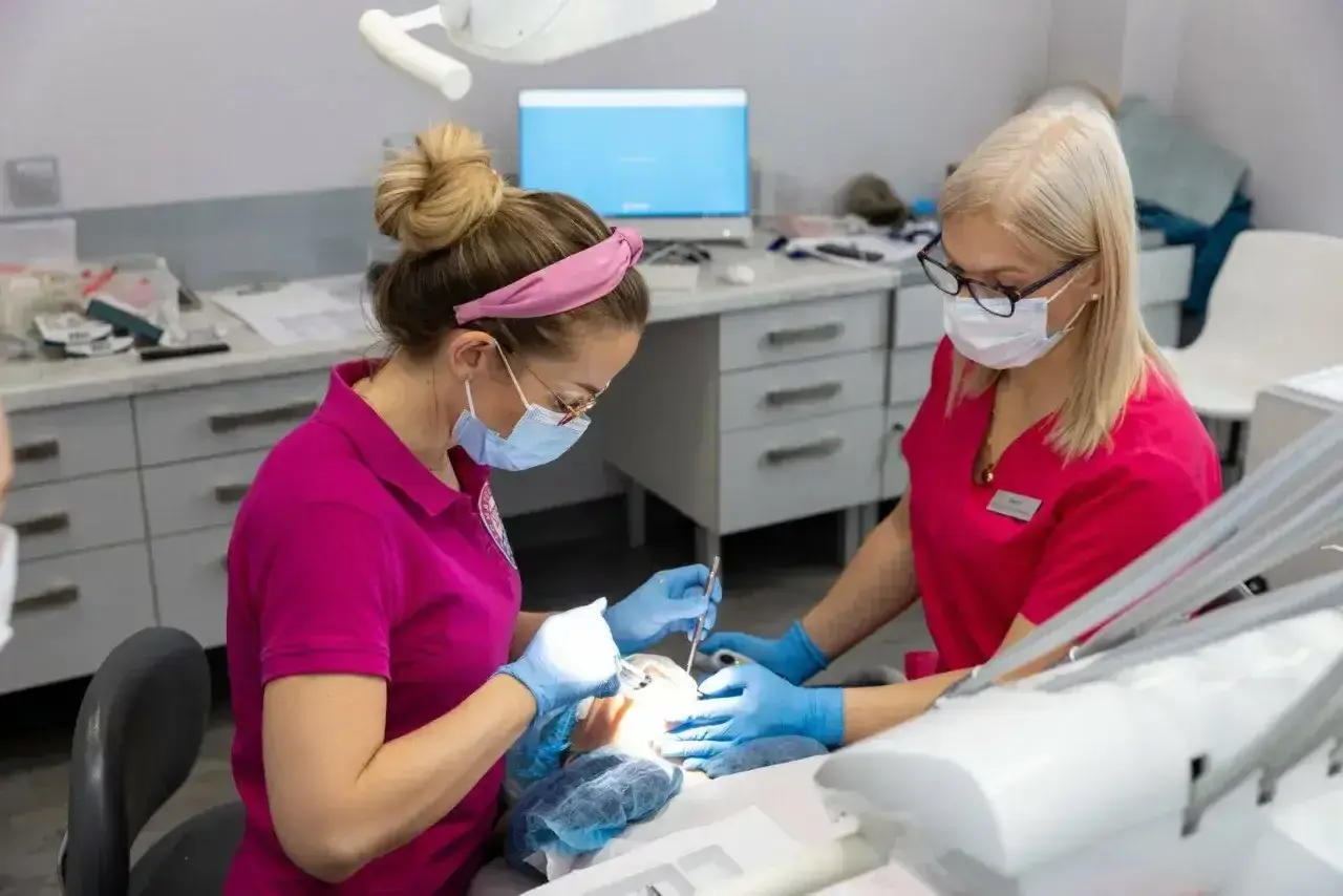 Dwie dentystki w maskach pracują przy pacjencie. Zastanawiasz się, ile schodzi znieczulenie od dentysty?