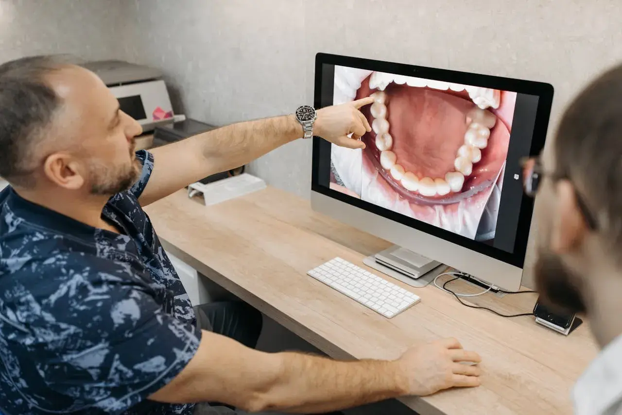 Dentysta pokazuje pacjentowi na ekranie powiększony obraz jamy ustnej, wskazując na zdrową kieszonkę dziąsłową.