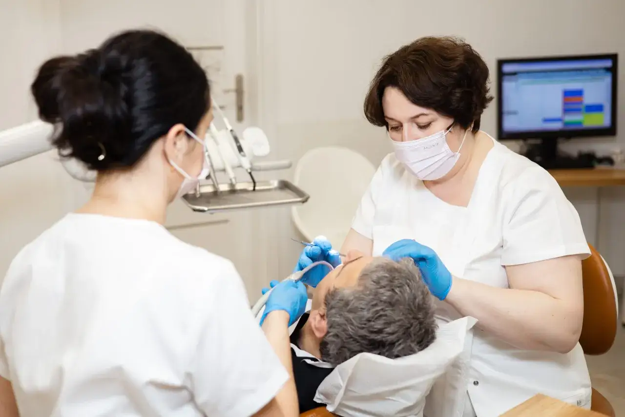 Pacjent z dentofobią przechodzi zabieg u dentysty. Dwie osoby w maskach i rękawiczkach pracują przy jego ustach.