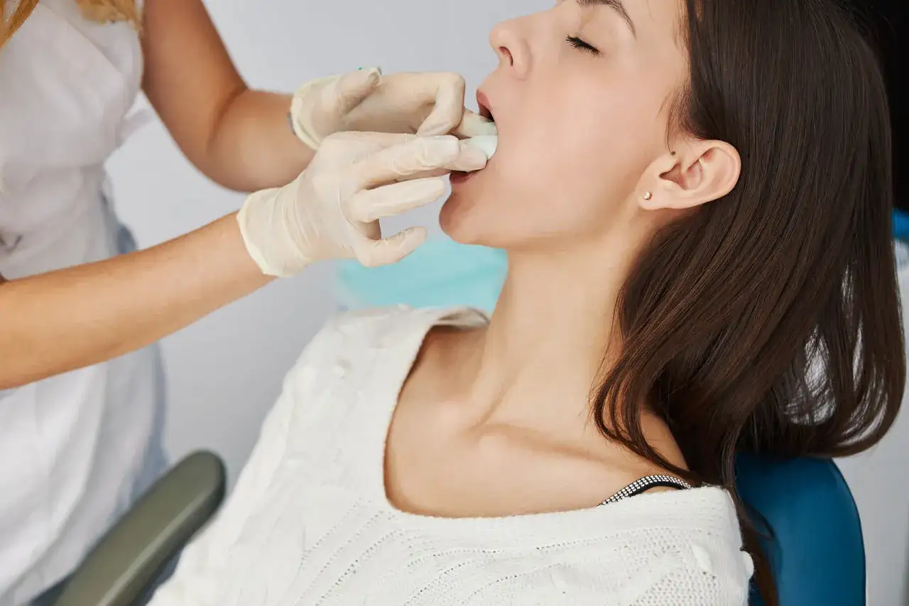 Lekarz w rękawiczkach wykonuje podcięcie wędzidełka u dorosłej pacjentki, która siedzi na fotelu dentystycznym.