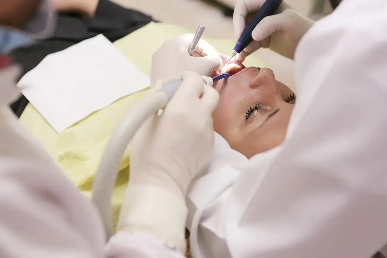 Dentysta wykonuje zabieg, który może być związany z przebiciem ropnia zęba. Pacjentka leży na fotelu, a lekarz używa narzędzi stomatologicznych.
