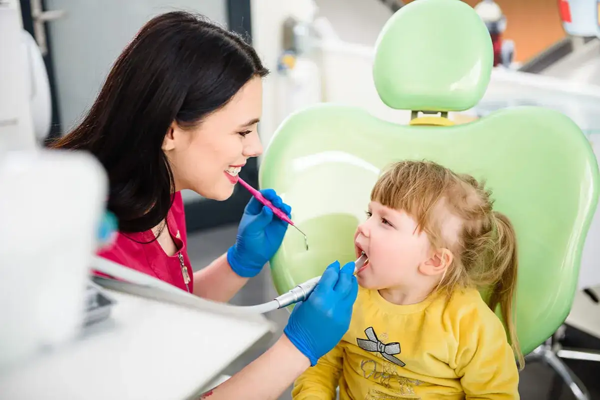 Uśmiechnięta dentystka wykonuje lakowanie zębów u małej dziewczynki.