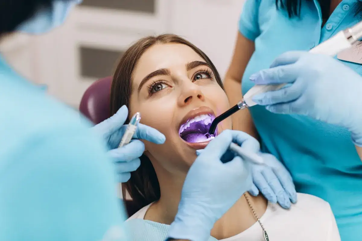 Dentysta utwardza światłem lampy plombę tymczasową w zębie pacjentki.