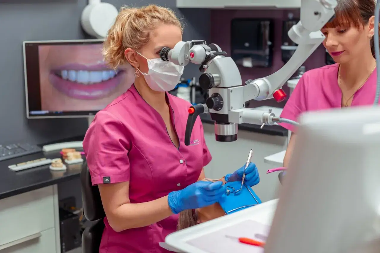 Dentystka w ciąży wykonuje leczenie kanałowe pod mikroskopem. Na ekranie widać zbliżenie pięknego uśmiechu.