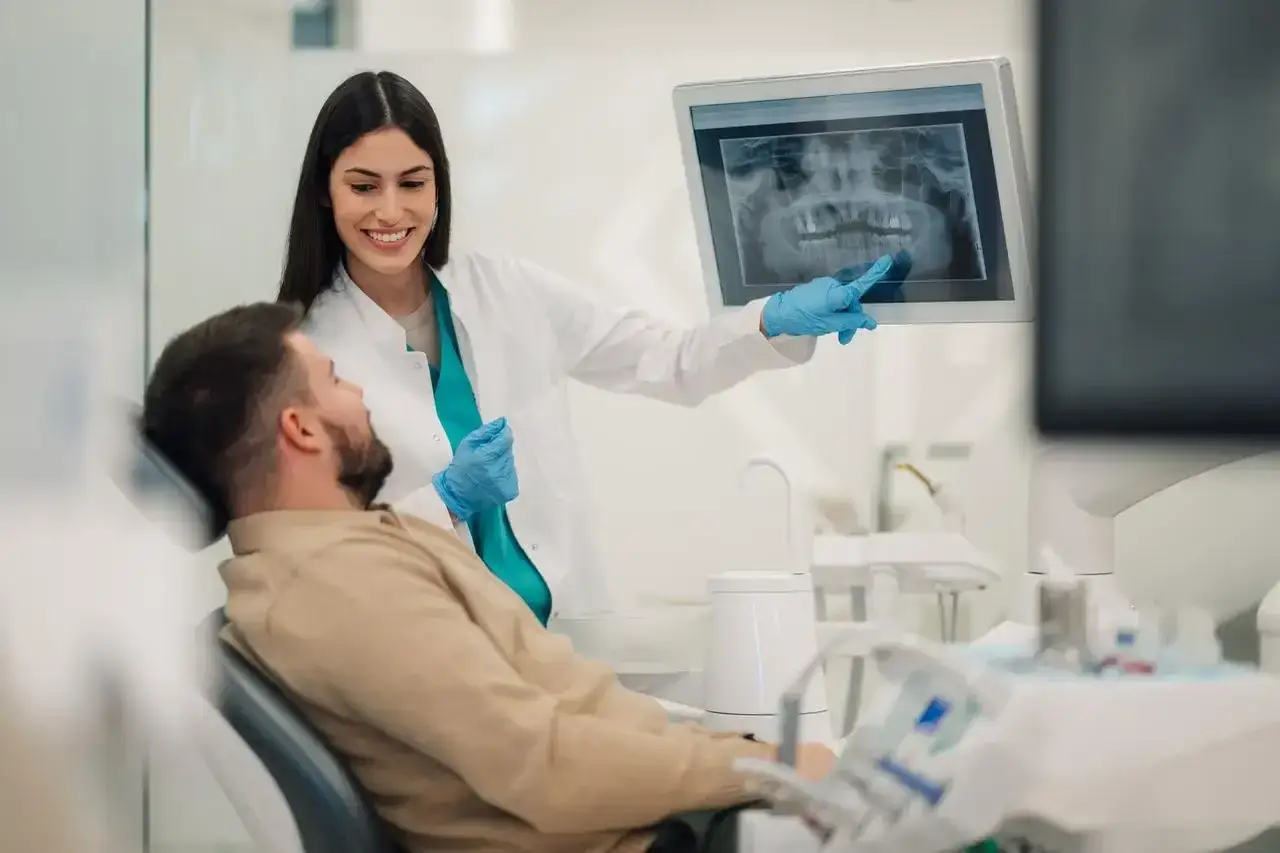 Dentystka pokazuje pacjentowi zdjęcie rentgenowskie zębów, omawiając plan leczenia. To inspiracja, jak zostać dentystą.